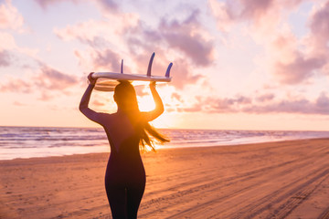 Beautiful young woman surf girl in wetsuit with surfboard on a beach at sunset or sunrise and ocean