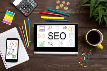 Tablet with web icon SEO on a wooden table with office tools.