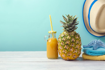 Pineapple, juice and beach towels on wooden table over mint background. Tropical summer vacation concept