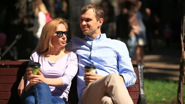 Man and woman sitting on a bench. A man and a beautiful woman on a date. They drink coffee and talk