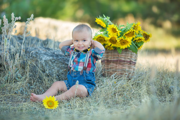 Cute handsome boy wearing jeans close to basket with sunflowers and stones.