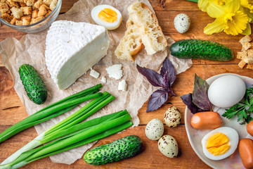 Products for snack on wooden background. Cheese, bread and croutons, cucumbers, green onion, boiled chicken and quail eggs, sausages, basil and parsley on the table.