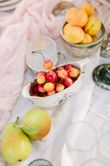 picnic, food, holiday concept - delicious fresh red and yellow cherries, pears, apricots on decorated table for the picnic, fruit plates and dishes, vegan food, white tablecloth, clean and fresh fruit