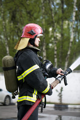 Obraz premium Fireman in fire fighting suit spraying water to fire surround