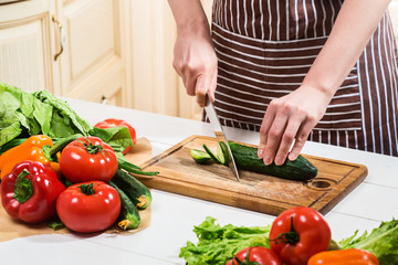 Young woman cooking in the kitchen at home. A woman cuts a cucumber and vegetables with a knife.