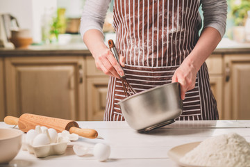 Young woman holding bowl with dough and whisk, closeup