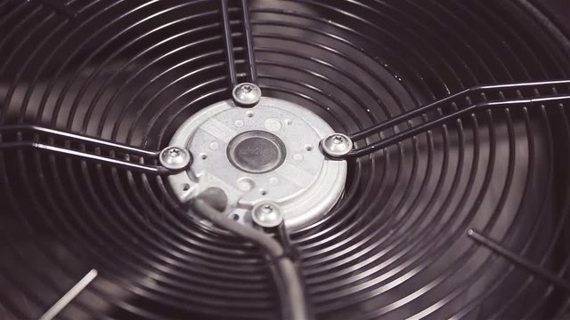Fan blades of air extractor, air conditioner, rotate at medium speed, are protected by grating. The system of screwing. Metallic blades closeup.