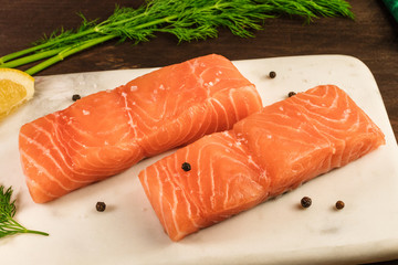 Two slices of salmon on dark background with drill sprigs