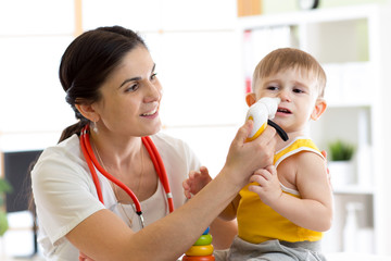 Female doctor pediatrician using nasal aspiration for child. Mucus suction patient kid baby.