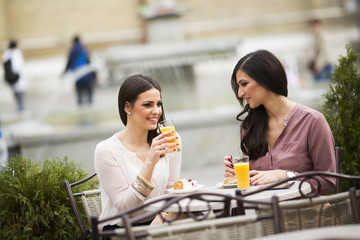 Two female friends sitting outside in a cafe and have fun