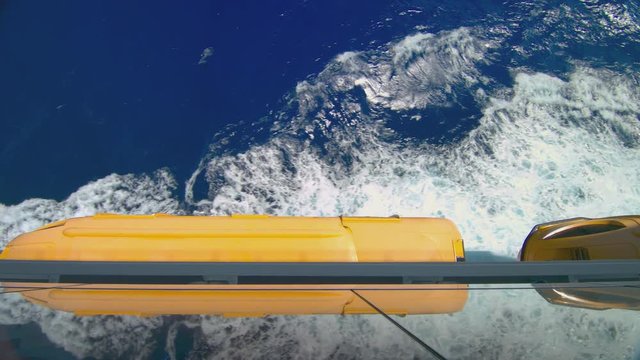View from Cruising Ship at Sea with Yellow Lifeboats Sailing through Exotic Blue Waters with Splashing White Waves