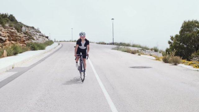 Beautiful women on a professional road bike in lycra black outfit and other triathlon equipment suffers trying to achieve her goal in solitude and exhaustion during hot and windy summer day.