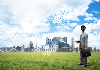 Camera headed man standing on green grass against modern cityscape
