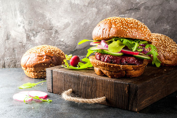 Healthy vegan burgers with beets, carrots, spinach, arugula, cucumber, radish and tomato sauce, whole grain buns on a rustic wooden board on a dark stone background, selective focus, copy space