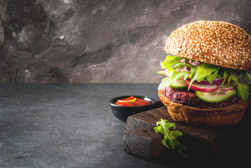 Healthy vegan burgers with beets, carrots, spinach, arugula, cucumber, radish and tomato sauce, whole grain buns on a rustic wooden board on a dark stone background, selective focus, copy space - obrazy, fototapety, plakaty