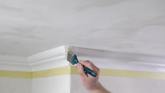 Painting walls and ceiling. A worker paints a ceiling moldings using a brush.