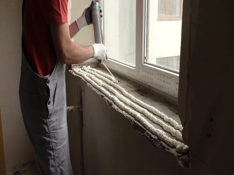 Worker is using a polyurethane foam for installation of window sill.