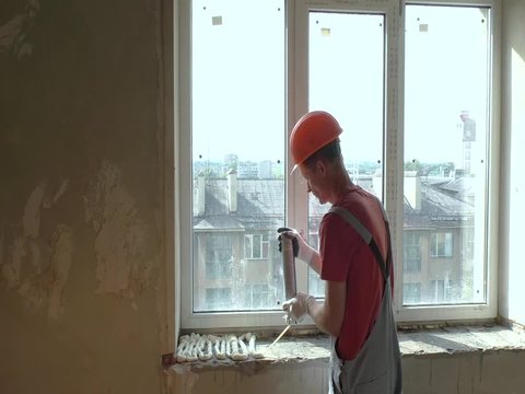 Worker is using a polyurethane foam for installation of window sill.