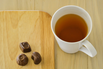 Tea cup and three chocolate candies on a wooden table