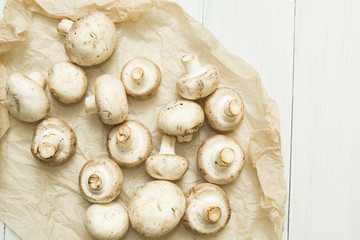 Freshly picked farm mushrooms champignons on white parchment paper. Organic vegetables.