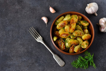 Young fried potatoes with garlic and dill on a black background