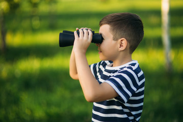 Little boy in a striped t-shirt looks through binoculars .Spring, sunny weather.