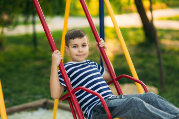 A little boy in a striped T-shirt is playing on the playground, Swing on a swing.Spring, sunny weather.