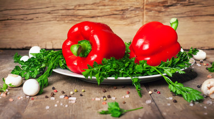 Two red bell peppers with fresh herbs and spices on wooden background. Rustic take..