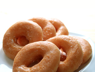 Closed up heap of sugar-glazed doughnuts served on white plate, isolated on white background 