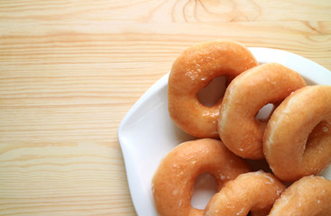 Top view of sugar-glazed doughnuts served on white plate on the wooden table, with free space for text and design 