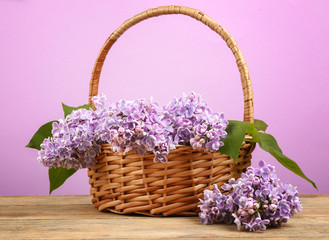 Fototapeta na wymiar Wicker basket with beautiful bouquet of lilac flowers on light table
