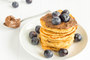 Stack of american pancake filled with hazelnut cream and blueberries on top. Hazelnut cream on spoon in the background.