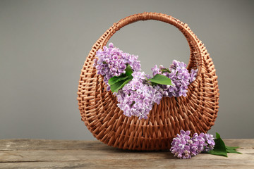 Fototapeta na wymiar Wicker basket with beautiful bouquet of lilac flowers on light table