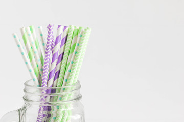 Fototapeta na wymiar Paper straws in blue, green, cyan and grey color placed on a trendy mason jar. Isolated shoot of party and wedding equipment. Collection of colorful straws.