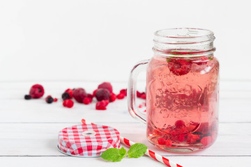 Raspberry healthy lemonade in an opened vintage mason jar with mint leaf and red paper straw placed on a white wooden board. Drink for the holidays.