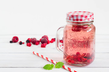 Raspberry healthy lemonade in an opened vintage mason jar with mint leaf and red paper straw placed on a white wooden board. perfect drink for a garden party.
