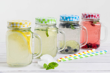 Homemade lemonade collection with colorful mason jars. Blueberry, raspberry, lemon and lime drinks with paper straws in blue, green, red and yellow color.