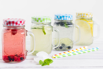 Homemade lemonade collection with colorful mason jars. Blueberry, raspberry, lemon and lime drinks with paper straws in blue, green, red and yellow color.