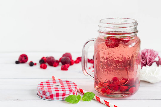 Raspberry healthy lemonade in an opened vintage mason jar with mint leaf and red paper straw placed on a white wooden board. Sugar free drink for the summer.