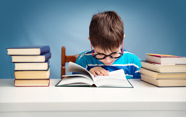 seven years old child reading a book at home. Boy studing at table on blue background