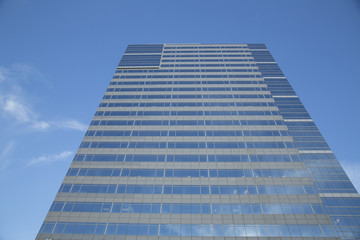 Fototapeta premium Dramatic Frontal Upward Skyward View Exterior Modern Reflective Glass Facade Skyscraper Tall Building in Business District Downtown Area, Against Blue Sky White Clouds, Daytime - West Coast USA