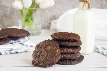 Stack of healthy cookies with dark chocolate on kitchen table. Milk and decoration in the backround.