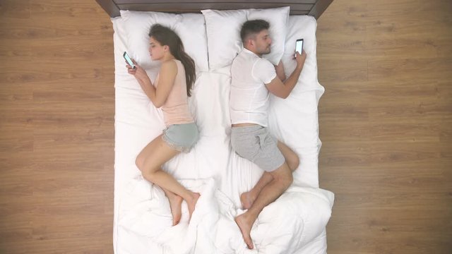 The Couple Lay With Phones In The Bed. View From Above