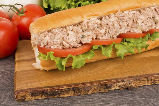 Close up on submarine tuna sandwich, vegetables in background.