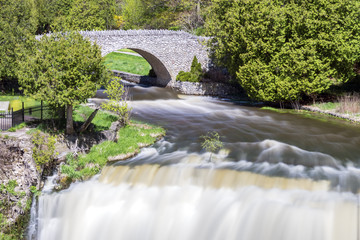 Fototapeta premium Stone bridge over river bend and waterfall, smooth flowing current