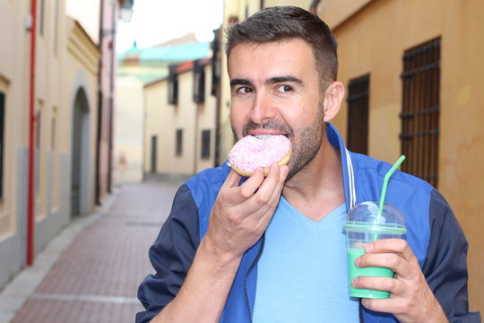 Man Eating A Donuts And Drinking A Shake Outdoors