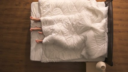 The man and woman have a sex under duvet. view from above
