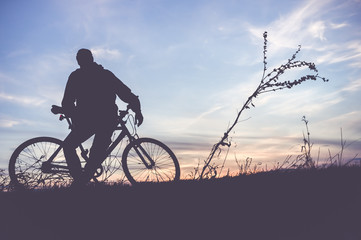 Obraz premium Silhouette of young man with a bicycle on the sunset