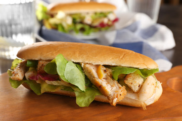Wooden board with chicken salad in hot dog bun on table