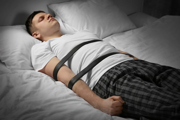 Young man tied up with belts in bed